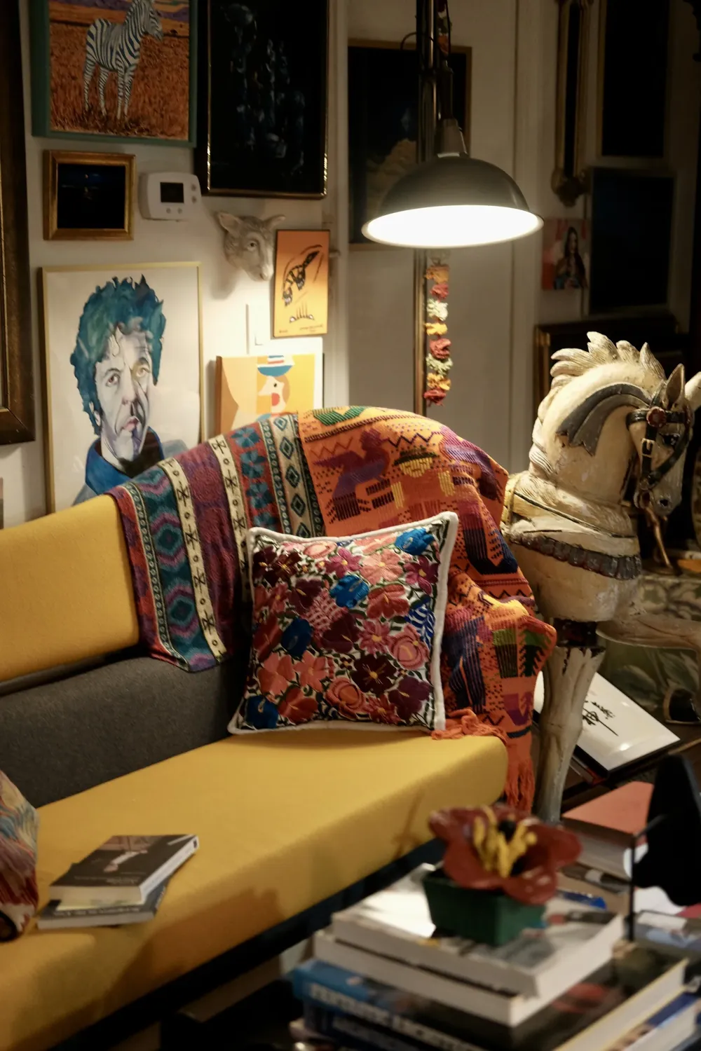 A real living room with a yellow sofa, layered textiles and a wall of original and vintage art